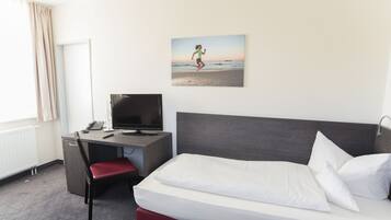 Una habitación de hotel con cama, escritorio, computadora, silla y ventana con cortinas.