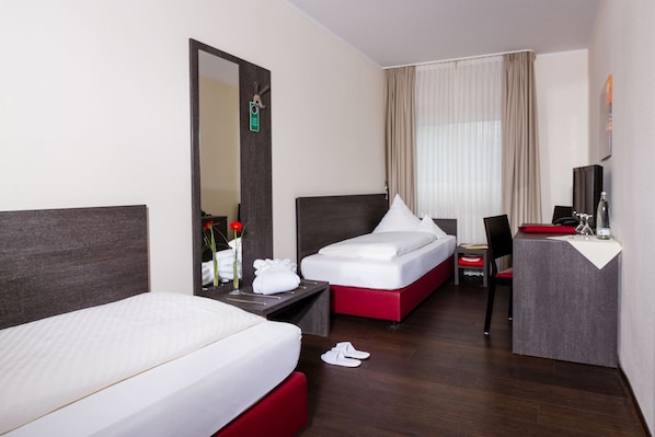 Habitación de hotel con dos camas, un escritorio, una silla, un espejo y una ventana con cortinas.