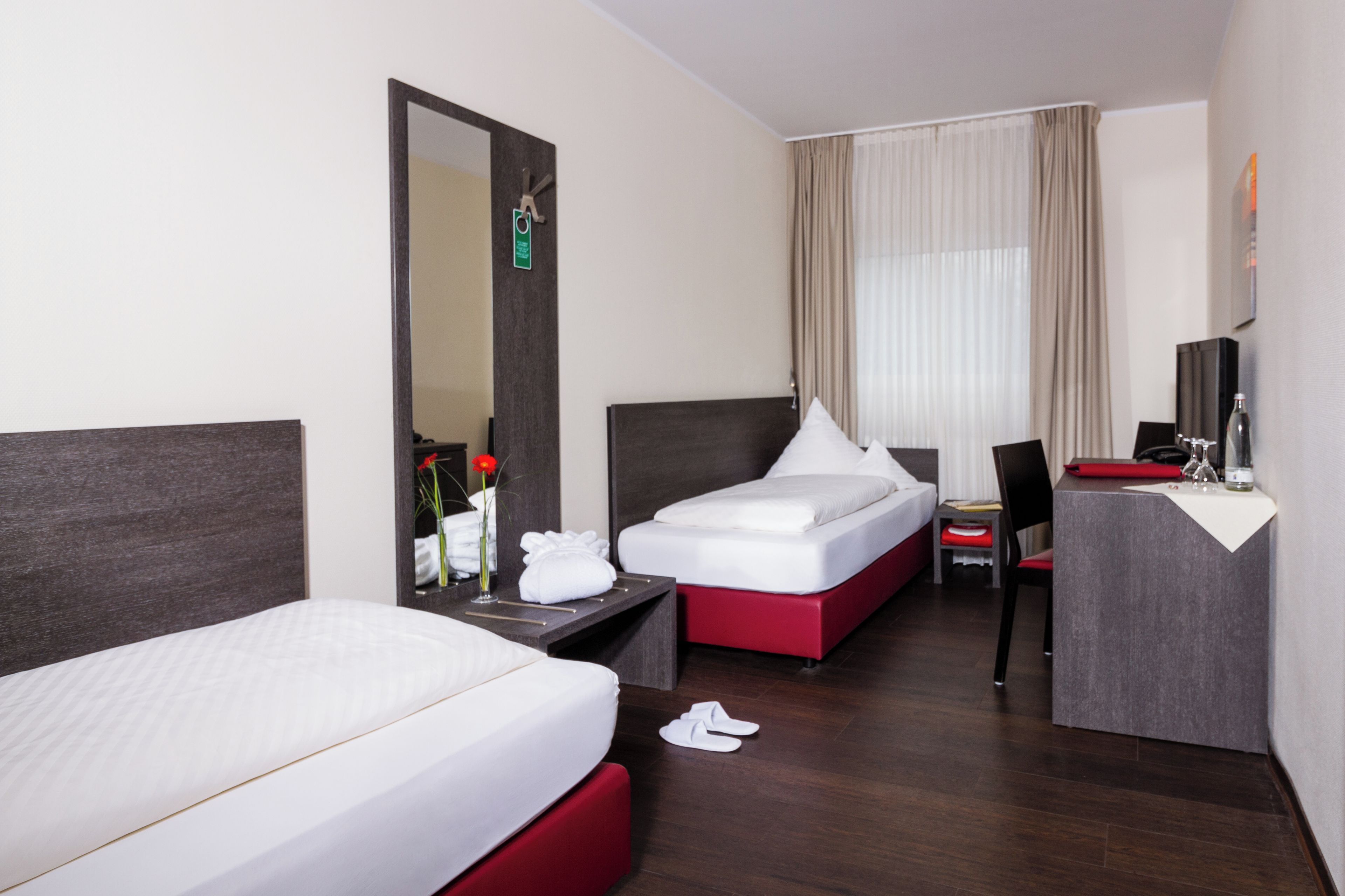 A hotel room with two beds, a desk, a chair, and a mirror.