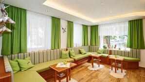A modern living room with a green sofa set, wooden tables, and a view of the street. - Schwaiger Hotel (EBEN)