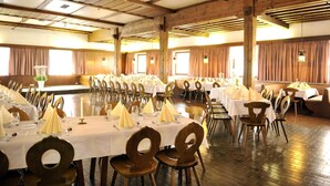 A large banquet hall with multiple round tables set for dining, wooden chairs, and a high ceiling with exposed beams. - Schwaiger Hotel (EBEN)