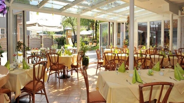 An indoor dining area with tables and chairs, covered by a glass roof, and surrounded by greenery. - Schwaiger Hotel (EBEN)
