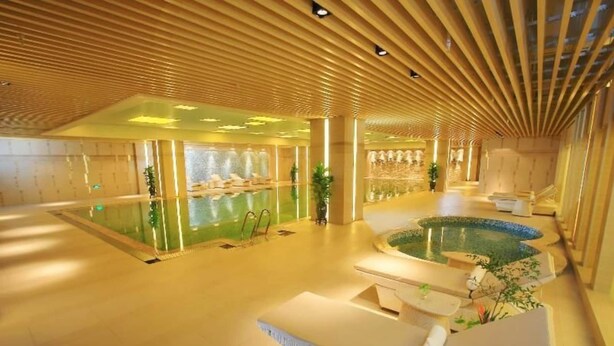 A spacious indoor area with a large pool, seating areas, and a modern ceiling design. - Grand NEW Century Hotel Fuyang (Hangzhou)