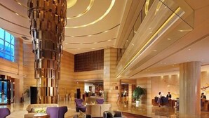 A modern hotel lobby with a central column, seating areas, and a reception desk. - Grand NEW Century Hotel Fuyang (Hangzhou)