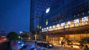 A hotel entrance with a modern glass facade, a pool area with lounge chairs, and a car parked in front. - Grand NEW Century Hotel Fuyang (Hangzhou)