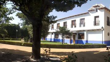 Un edificio de dos pisos con fachada blanca y detalles azules, rodeado de árboles y un césped bien cuidado.