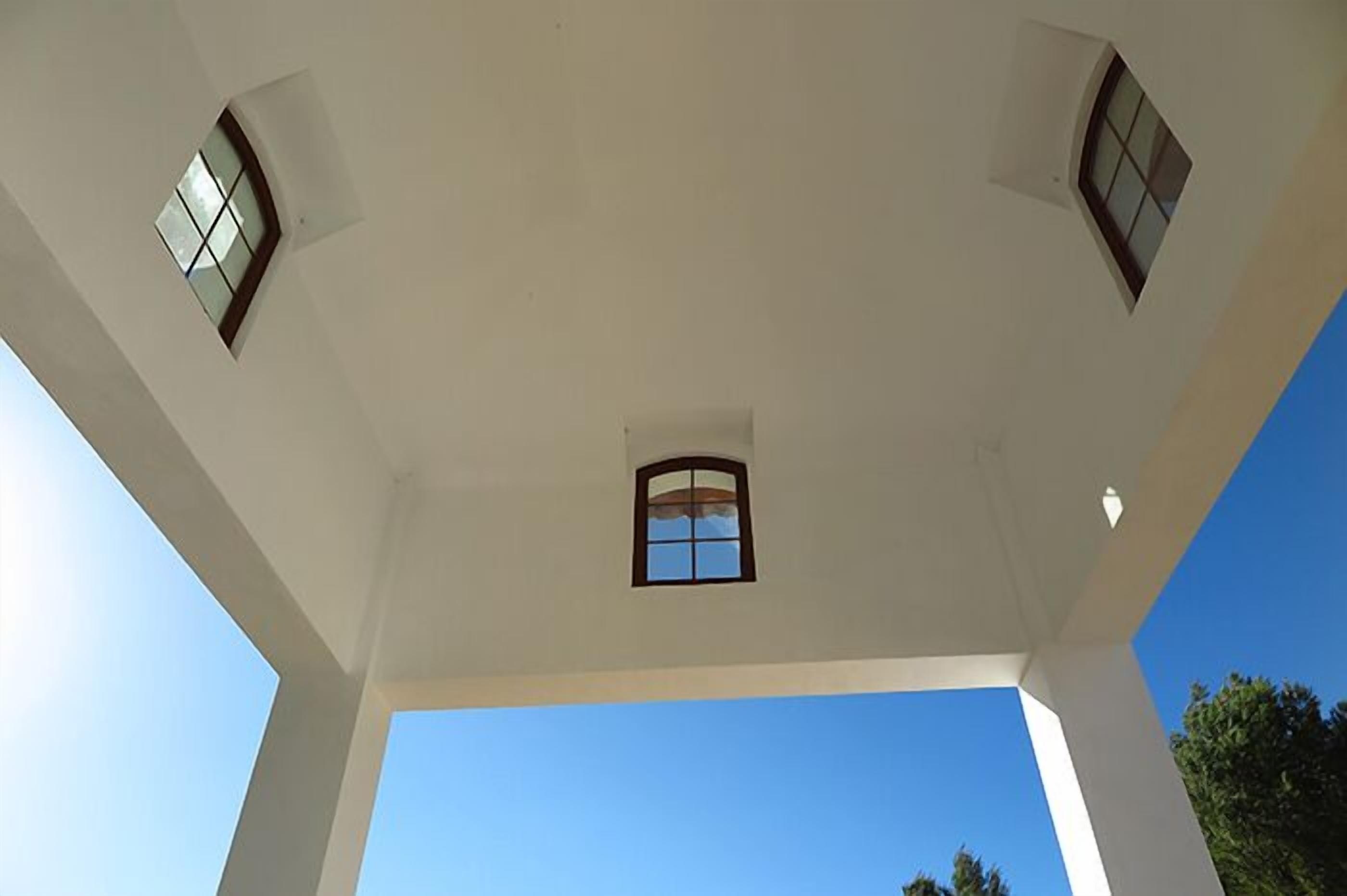 A high ceiling with three windows and a clear blue sky visible through the windows.