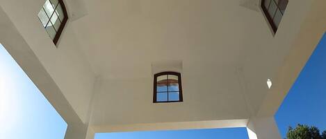 A high ceiling with three windows and a clear blue sky visible through the windows.