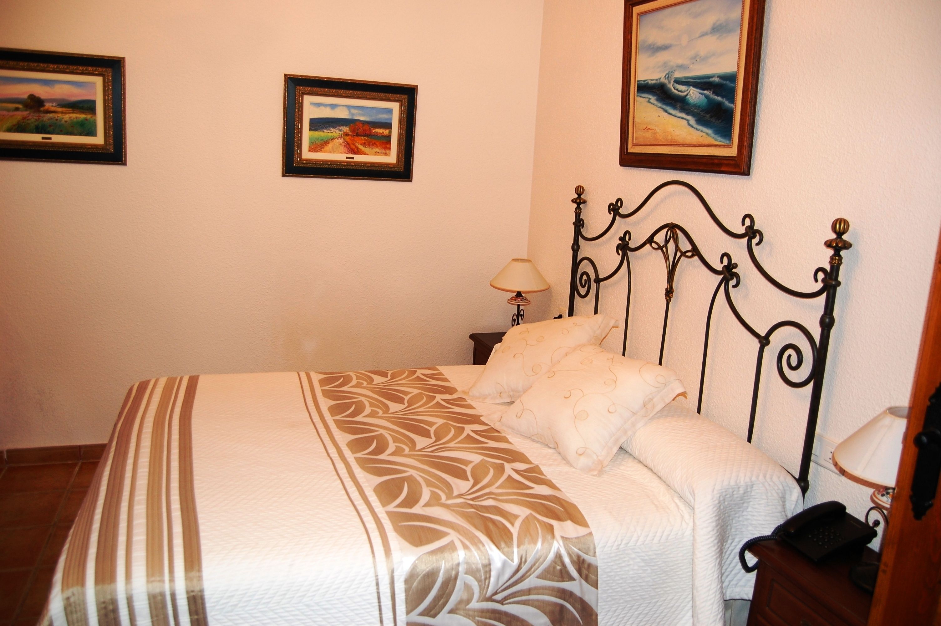 A neatly made bed with a patterned bedspread, a bedside table with a lamp, and two framed pictures on the wall.