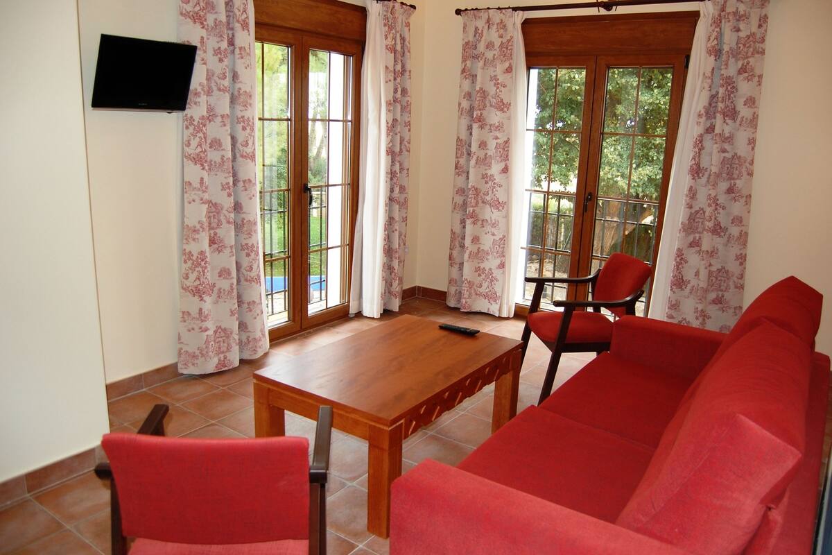 A room with a wooden table, red chairs, a red sofa, and a TV on the wall.