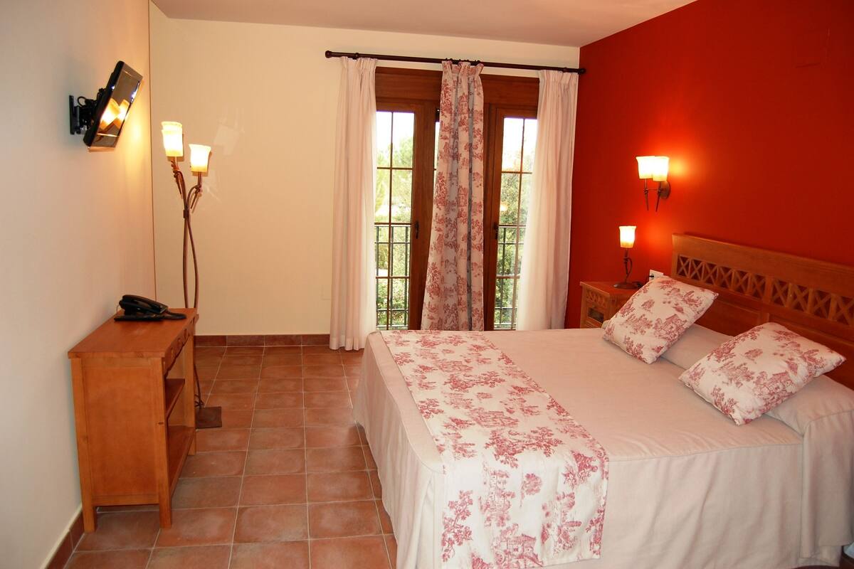 A bedroom with a bed, bedside lamps, a wooden nightstand, a telephone, and a window with curtains.