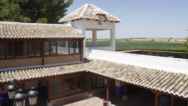 A traditional building with tiled roofs and wooden windows, featuring a covered patio area and a view of the countryside. - Hotel El Cortijo de Daimiel (Daimiel)