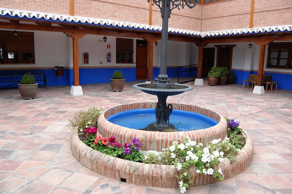 Une cour intérieure avec une fontaine centrale, entourée de plantes et de fleurs en pot.