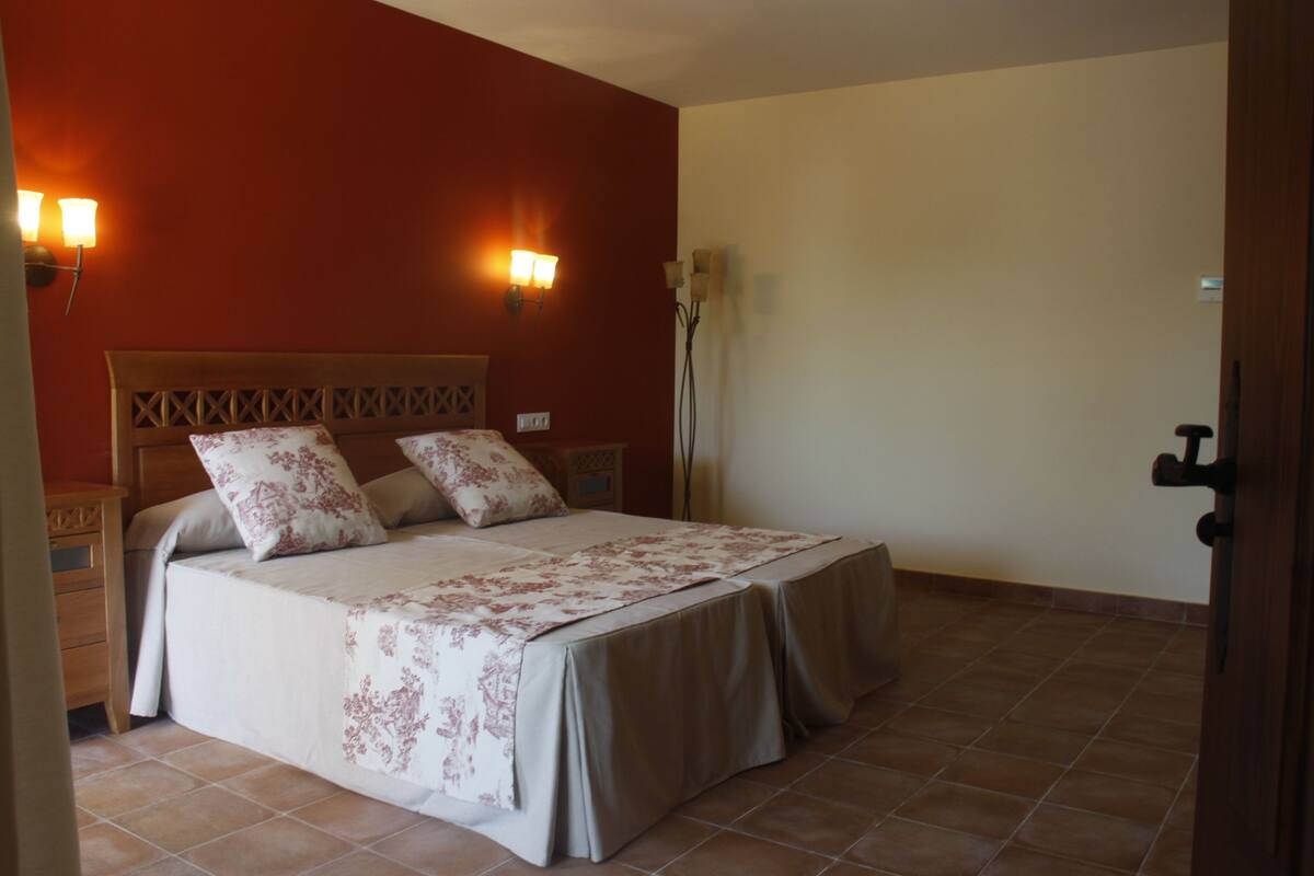A bedroom with a bed, two bedside tables, a nightstand, and a wall-mounted lamp.