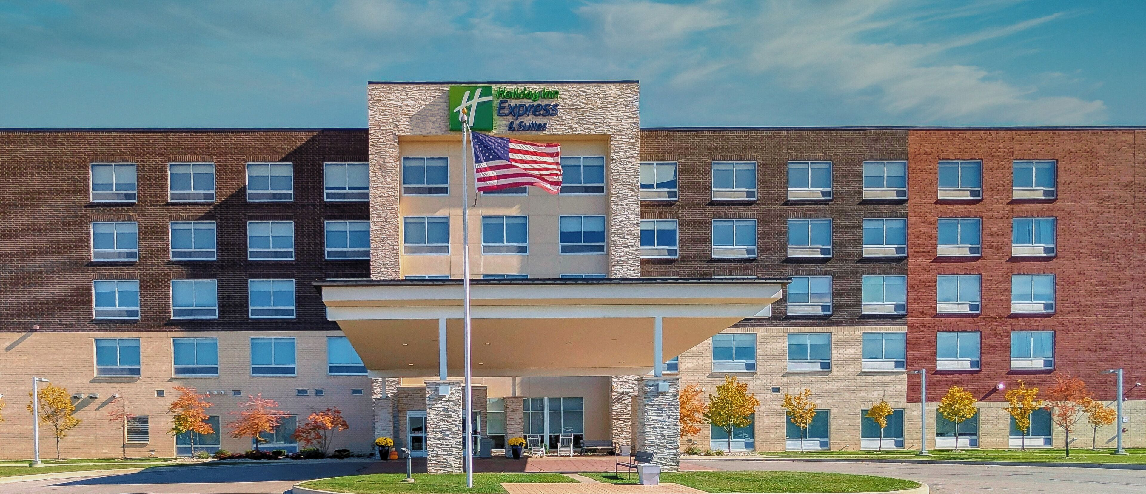 Edificio de Holiday Inn Express & Suites con un acceso cubierto, varias ventanas y una bandera estadounidense.