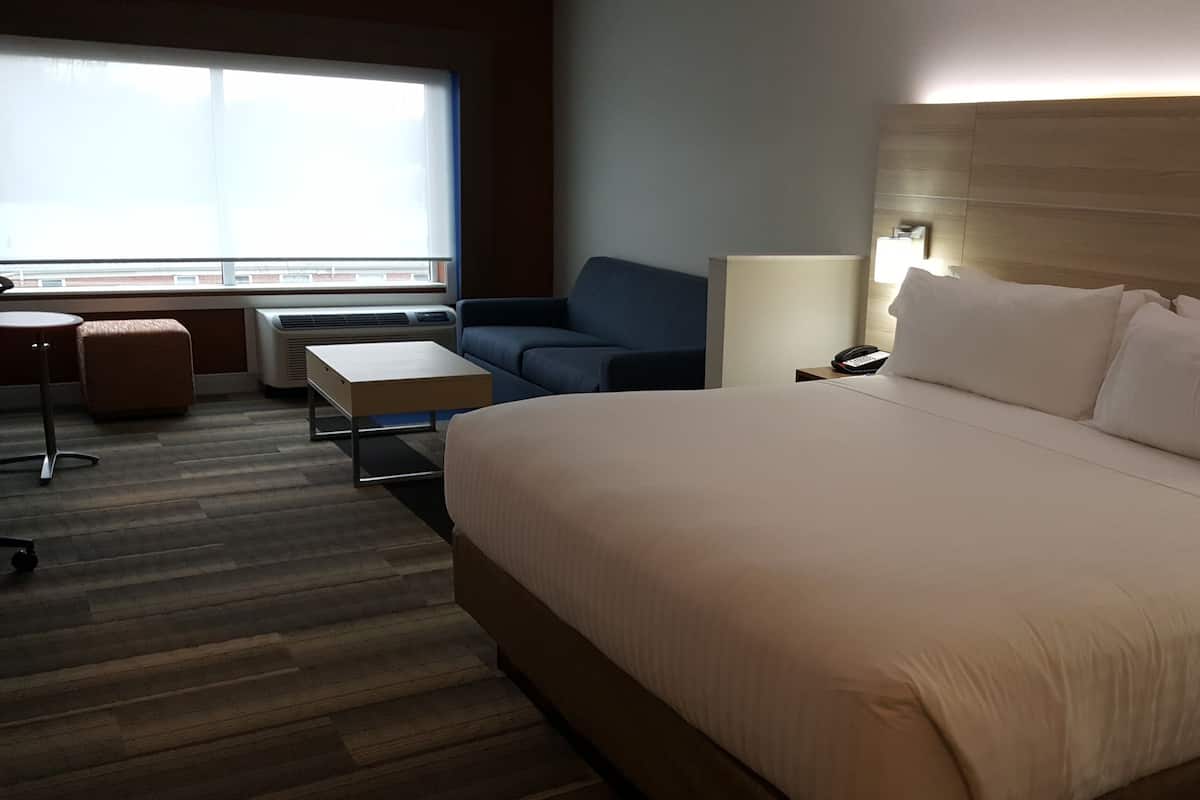 Ein Hotelzimmer mit einem großen Bett, einem Schreibtisch, einem Stuhl, einer Lampe und einem Fenster mit Aussicht.