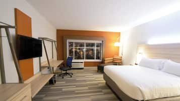 A hotel room with a bed, desk, chair, TV, window, and lamp.