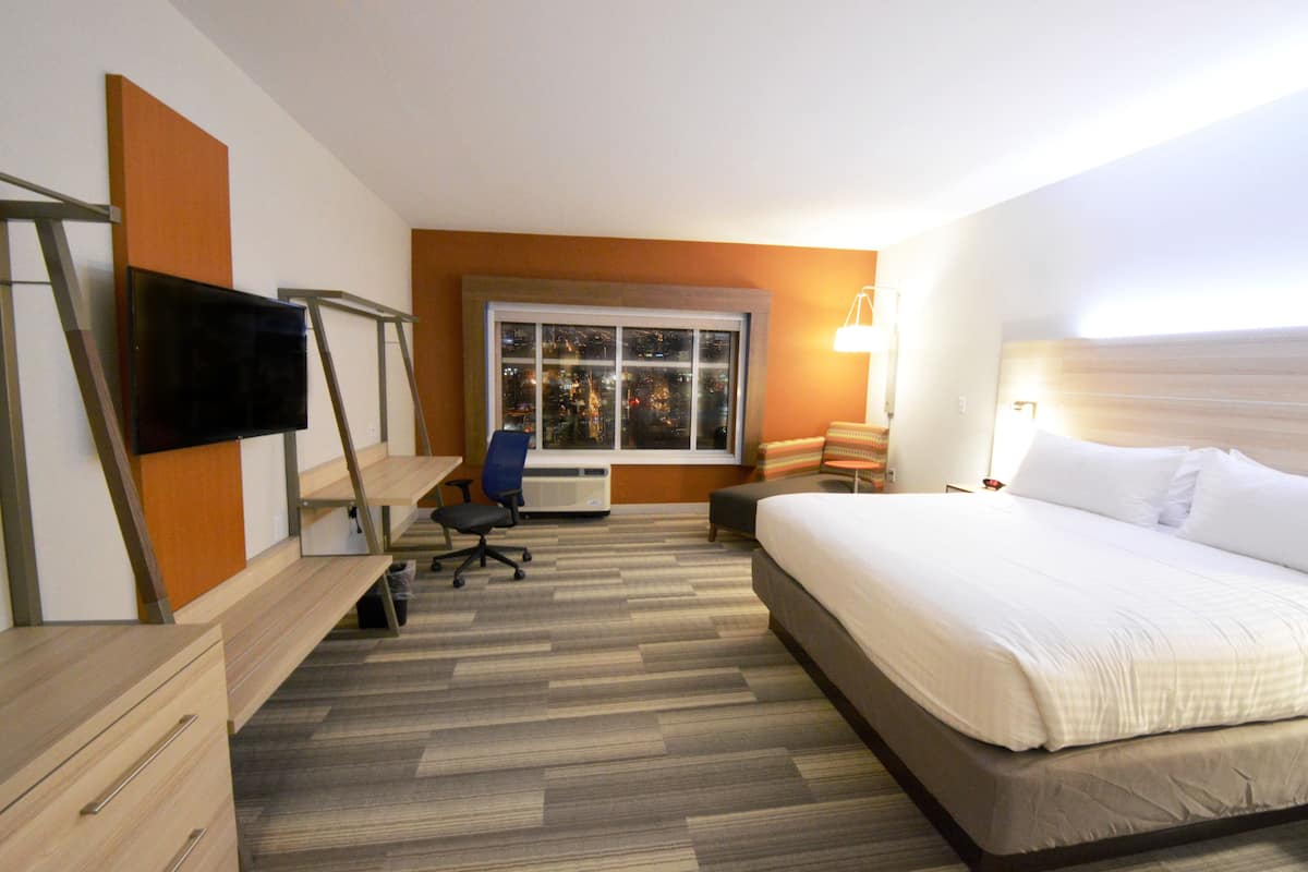 Ein Hotelzimmer mit Bett, Schreibtisch, Stuhl, Fernseher, Fenster und Lampe.