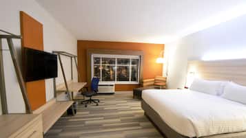 Habitació d'hotel amb llit, escriptori, cadira, televisió, finestra i làmpada.