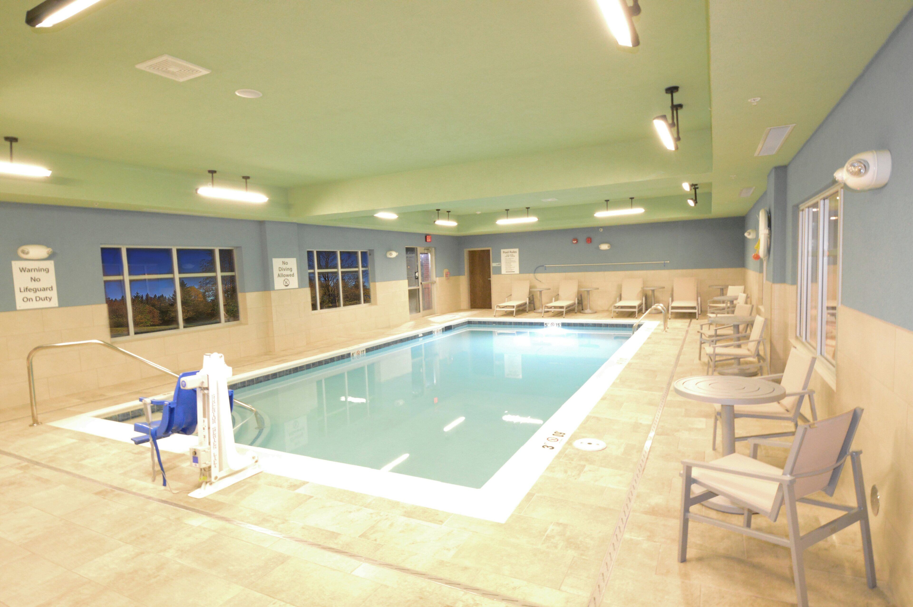 An indoor swimming pool with a lifeguard chair, pool rules sign, and seating area.