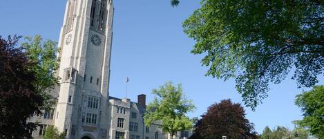 A historic stone building with a clock tower, surrounded by trees and a well-maintained lawn.