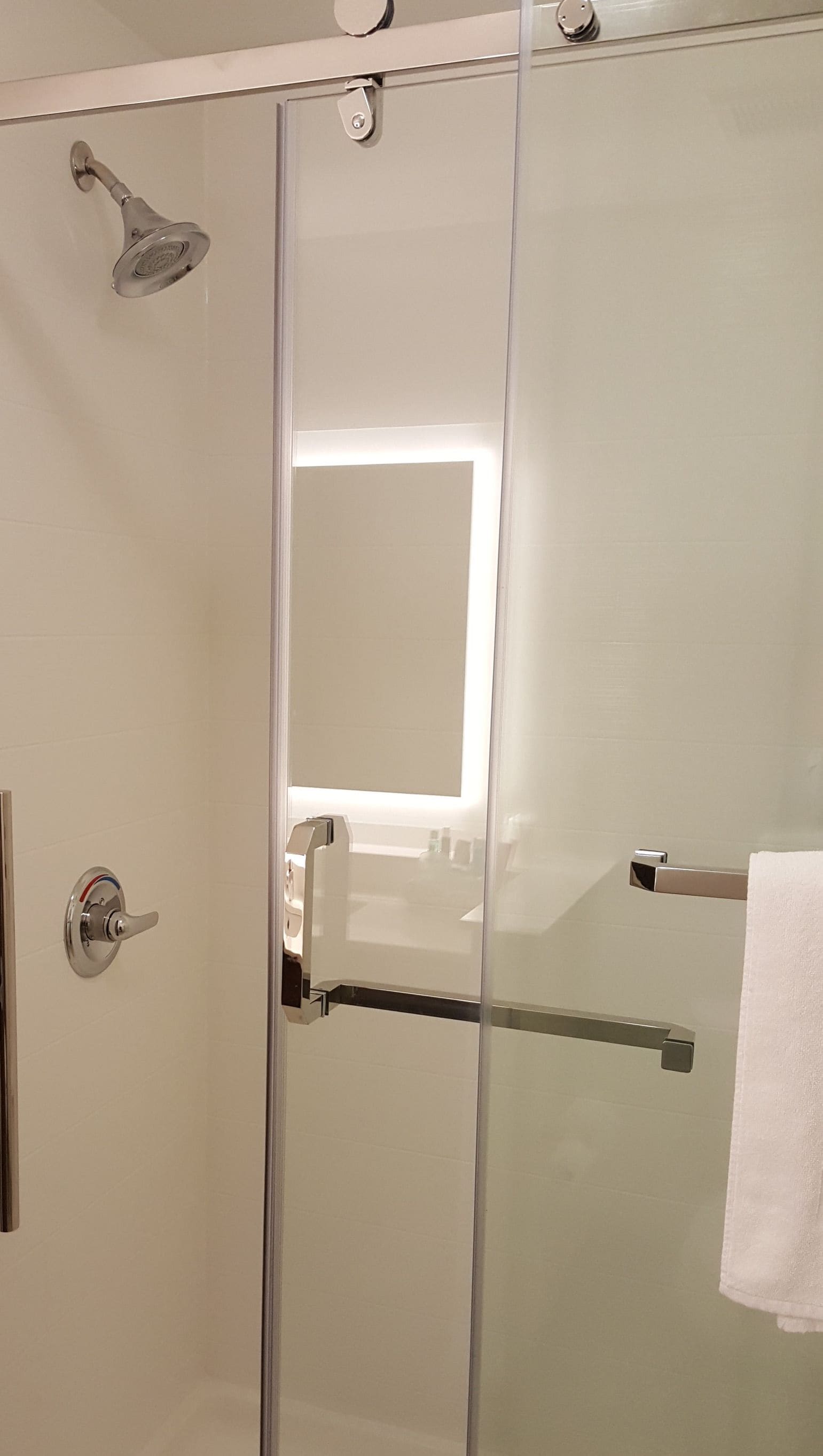 Una ducha con cerramiento de vidrio, cabezal de ducha de mano y un perchero para toallas.