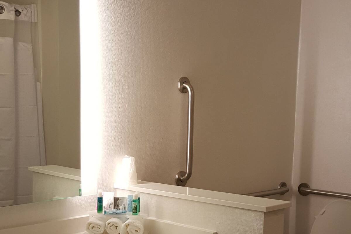 Ein Badezimmer mit einem weißen Waschbecken, einem Spiegel, einer Toilette und einer Handstange.