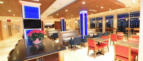Un restaurant avec des banquettes et des tables, un pilier bleu et un écran de télévision.