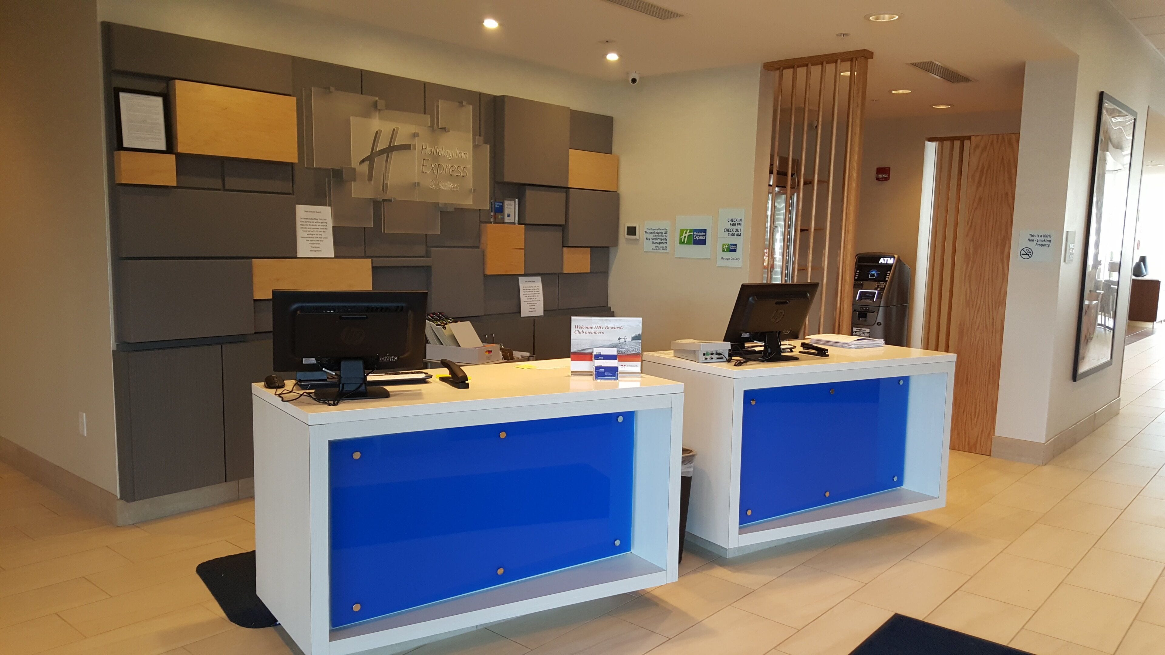 Un mostrador de recepción de hotel con dos estaciones de computadoras, un letrero de Holiday Inn Express & Suites y un cajero automático.