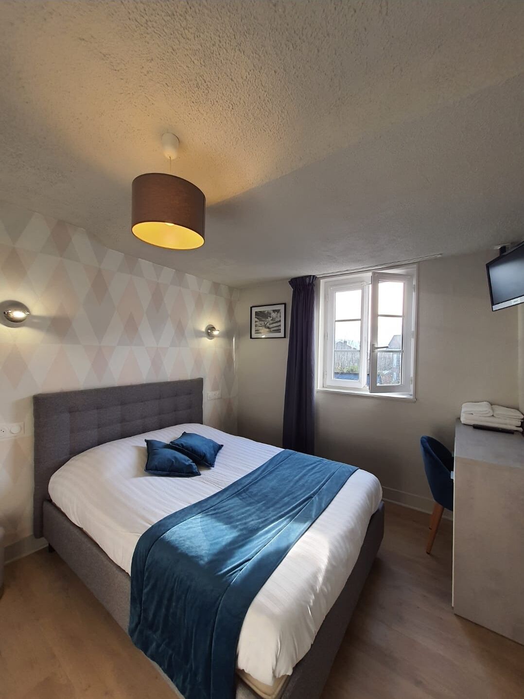 A bedroom with a bed, a desk, a chair, a window, and a television.