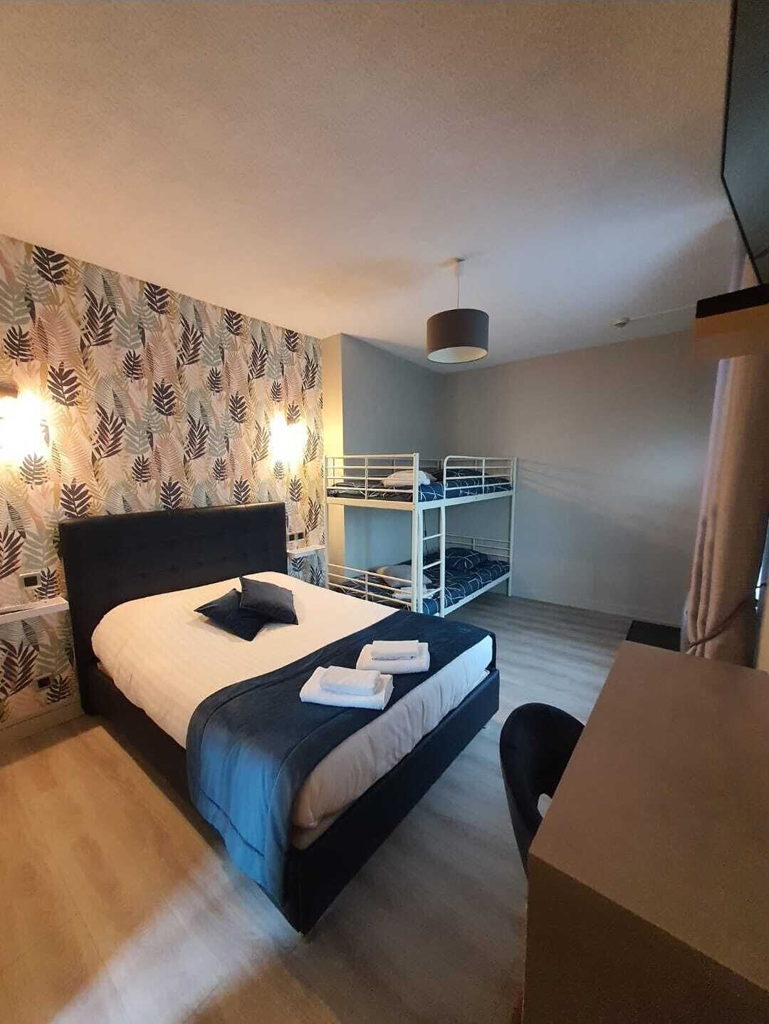 Pieni hotellihuone, jossa on yksi sänky, kerrossänky, työpöytä ja tuoli.