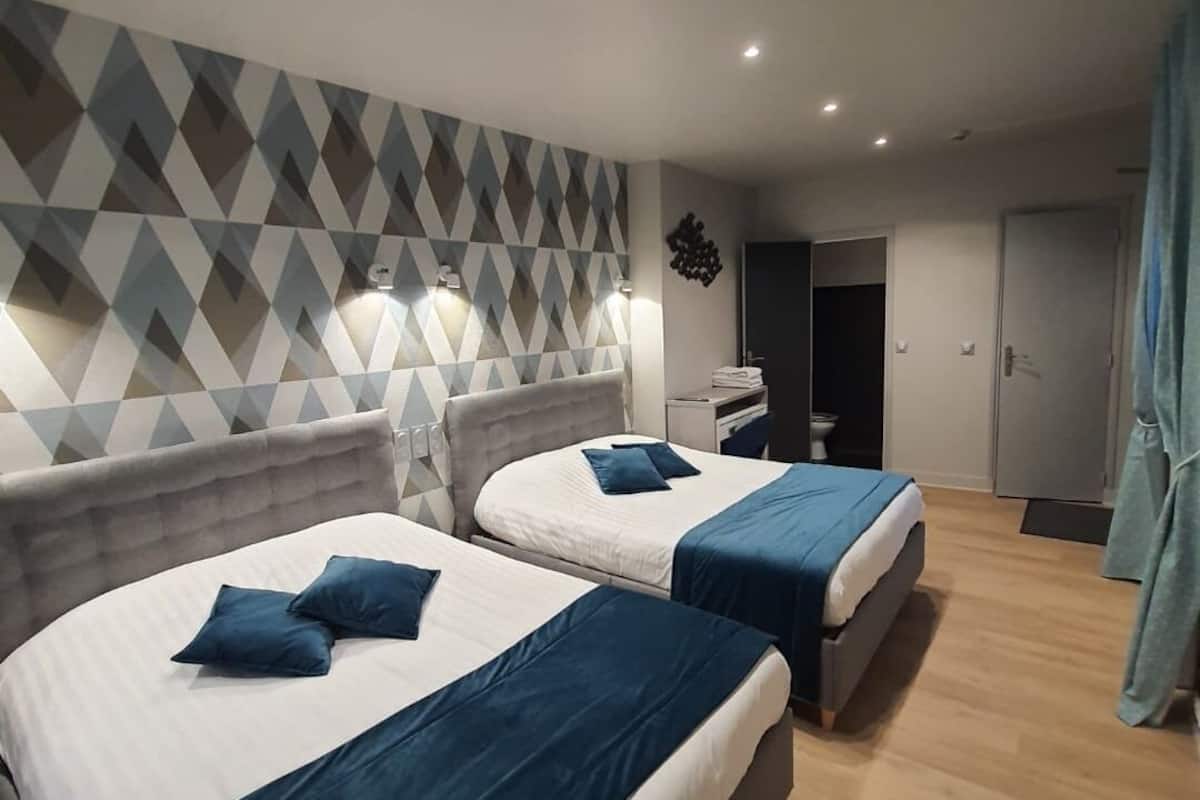 A hotel room with two beds, a geometric-patterned wall, and a wooden floor.