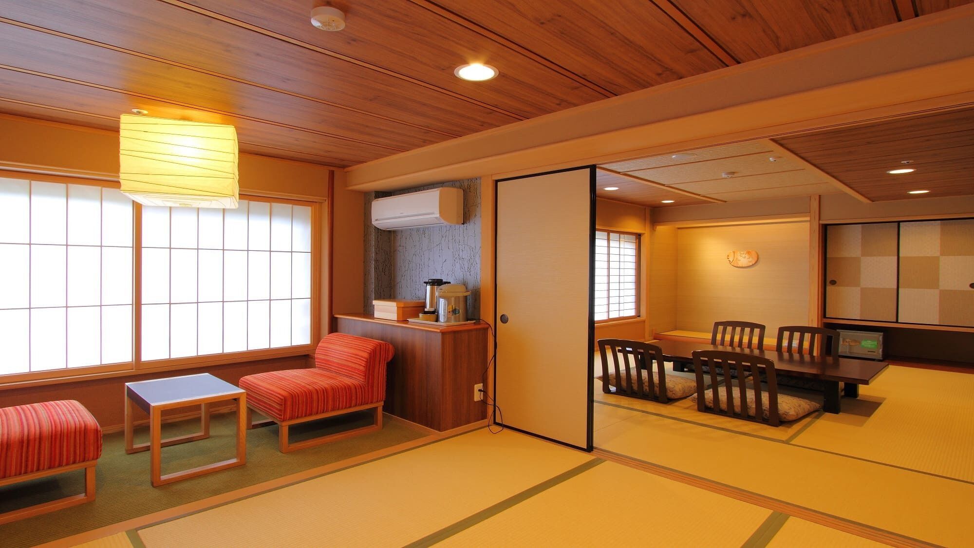 A traditional Japanese room with tatami flooring, a low table with chairs, a sliding door, and a window with shoji screens.