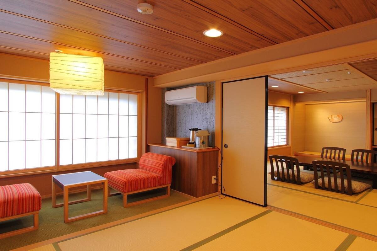 A traditional Japanese room with tatami flooring, a low table with chairs, a sliding door, and a window with shoji screens.