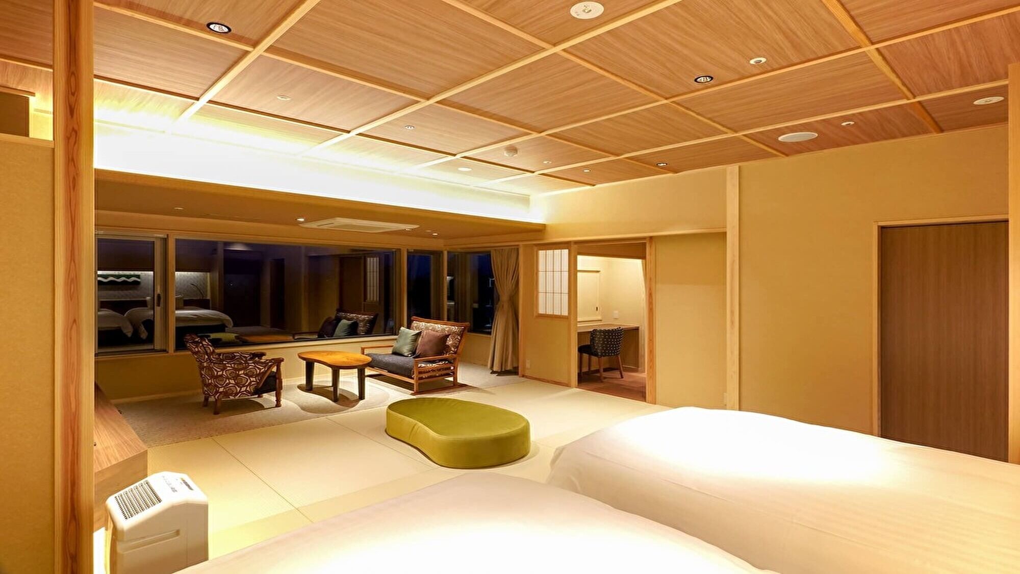 A hotel room with a large bed, a seating area with chairs and a table, a window with a view, and a wooden ceiling.