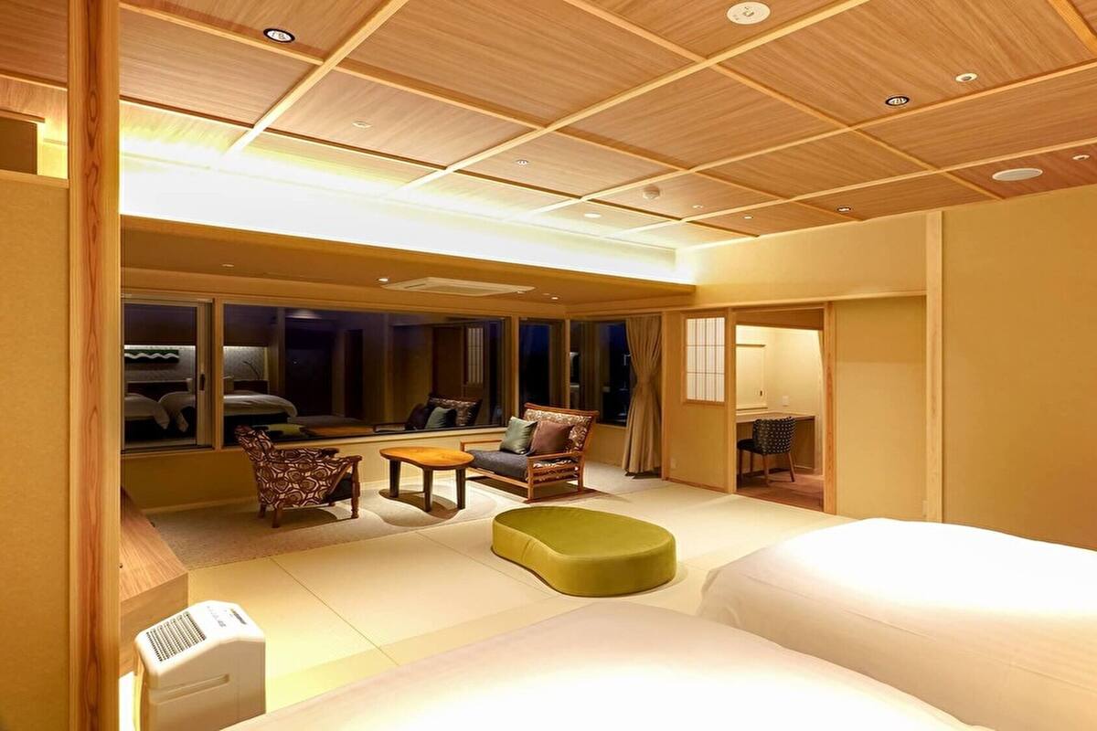 A hotel room with a large bed, a seating area with chairs and a table, a window with a view, and a wooden ceiling.