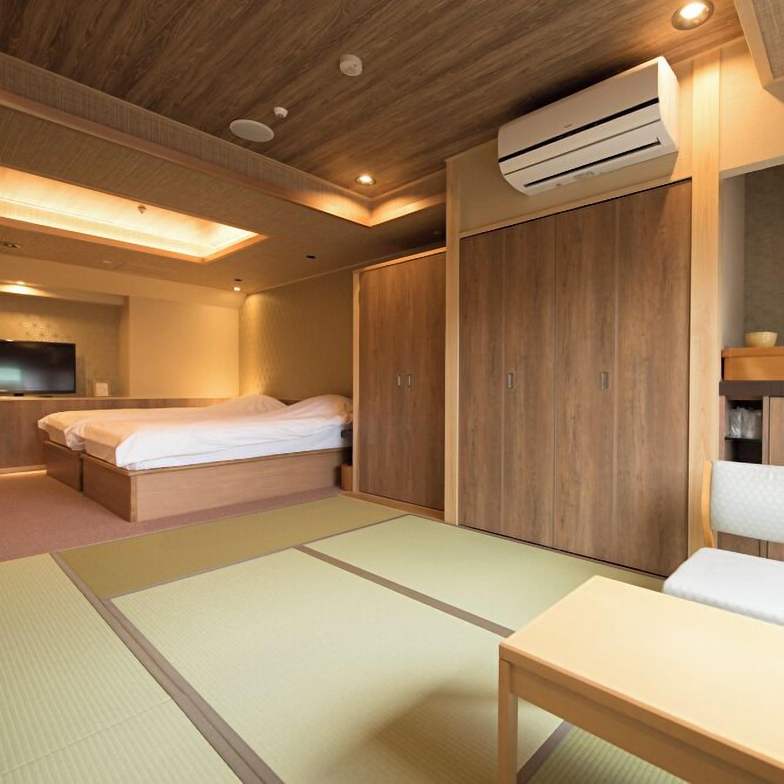 A hotel room with a bed, a wooden wardrobe, a small table, a TV, and an air conditioning unit.