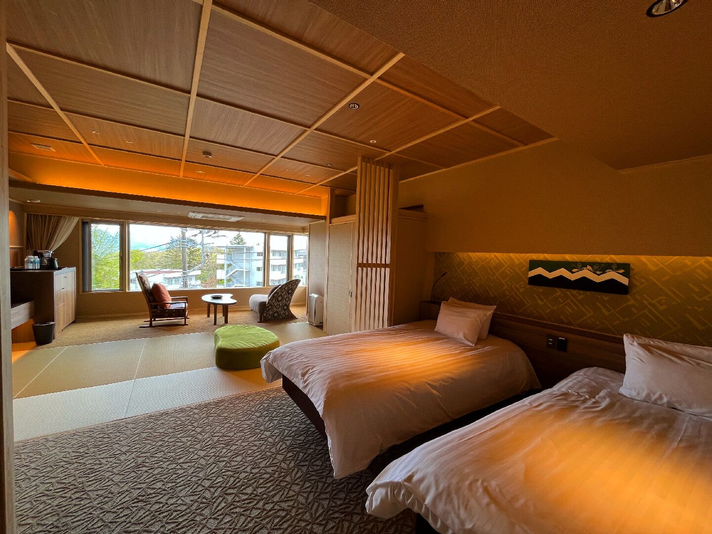 A hotel room with two beds, a seating area with a table, and a large window offering a view.