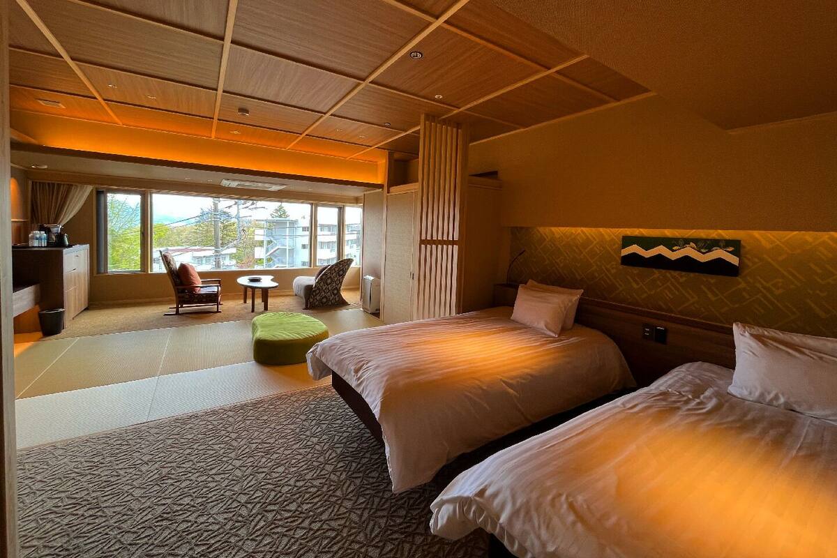 A hotel room with two beds, a seating area with a table, and a large window offering a view.