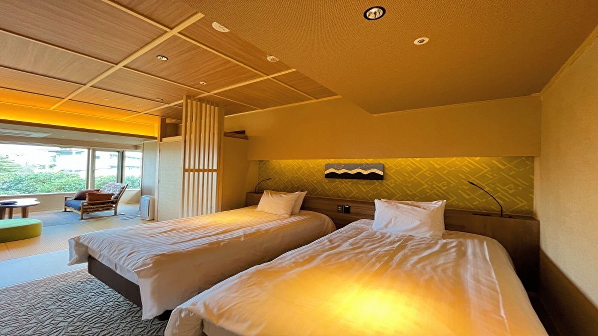 A hotel room with two beds, a sofa, and a view of greenery outside.