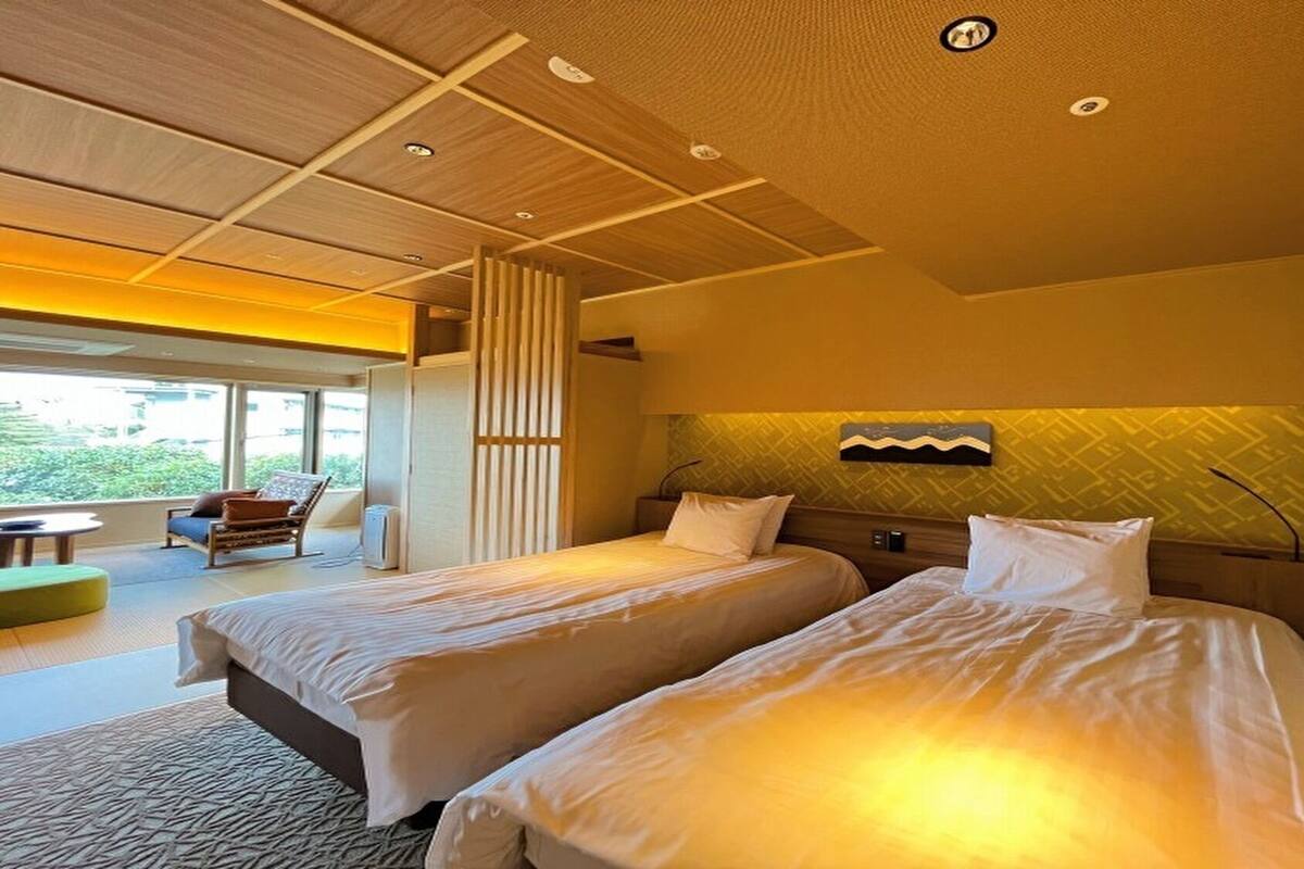 A hotel room with two beds, a sofa, and a view of greenery outside.