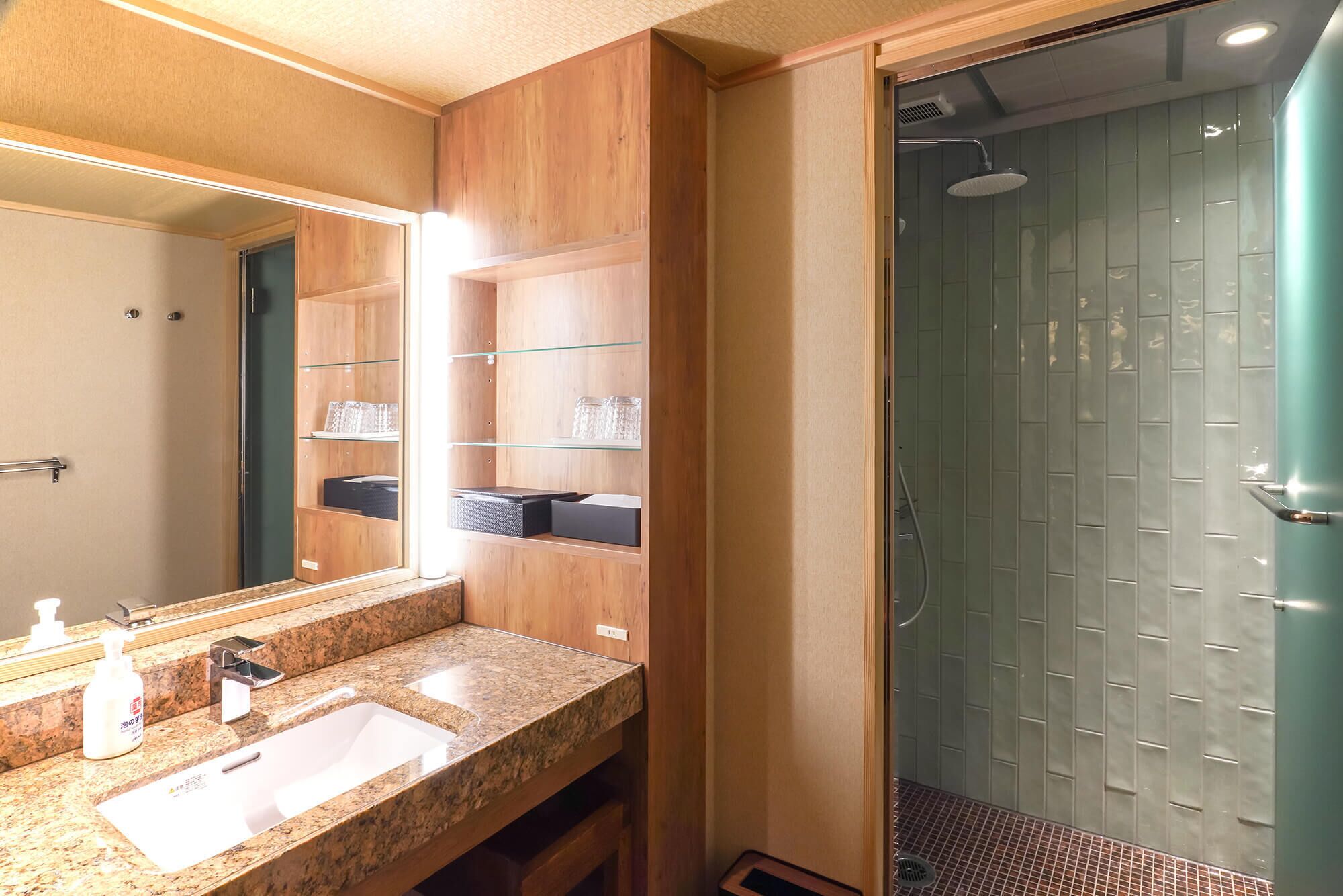 Un baño con encimera de granito, lavamanos, espejo y ducha con paredes de vidrio.