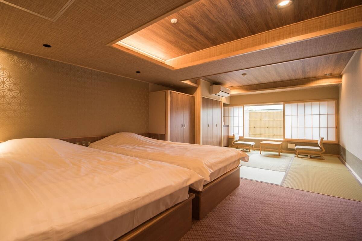 A hotel room with a large bed, wooden ceiling, and a view of a traditional Japanese room.