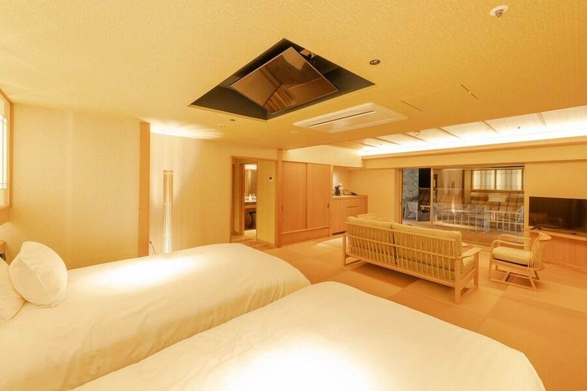 A hotel room with two beds, a seating area, a television, and a window.