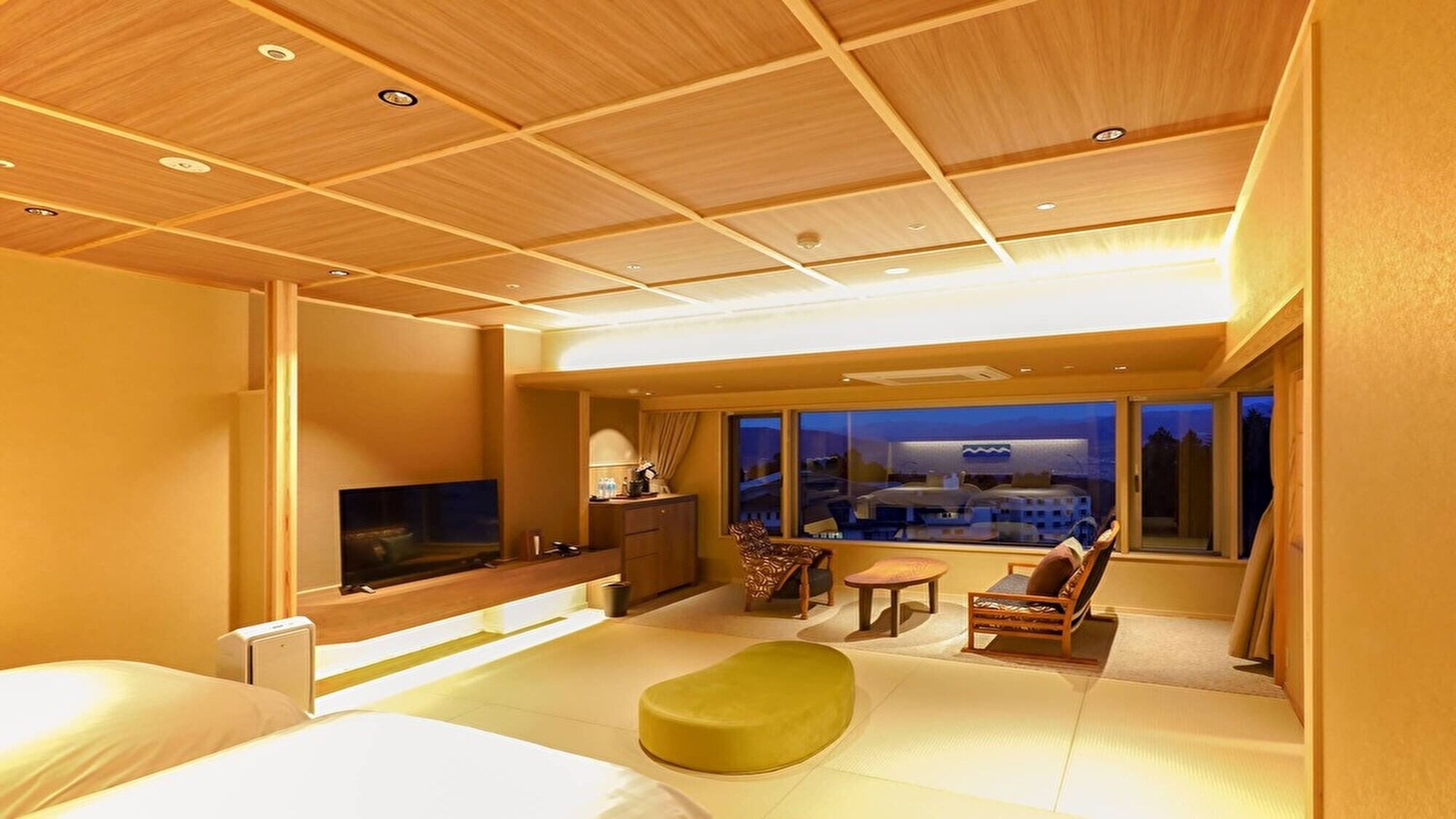 A hotel room with a bed, a TV, a desk, a chair, a sofa, and a large window with a view.