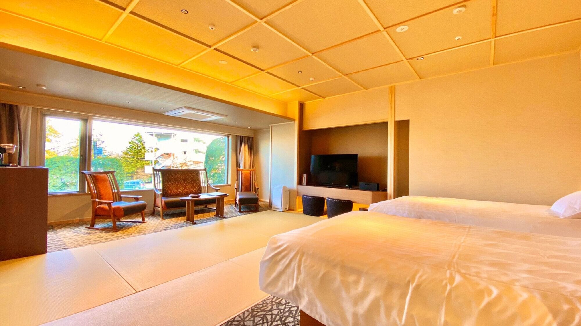 A hotel room with a large bed, a TV, a seating area with chairs, and a view through the window.