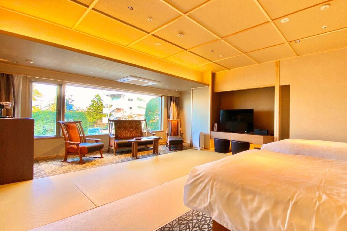 A hotel room with a large bed, a TV, a seating area with chairs, and a view through the window.