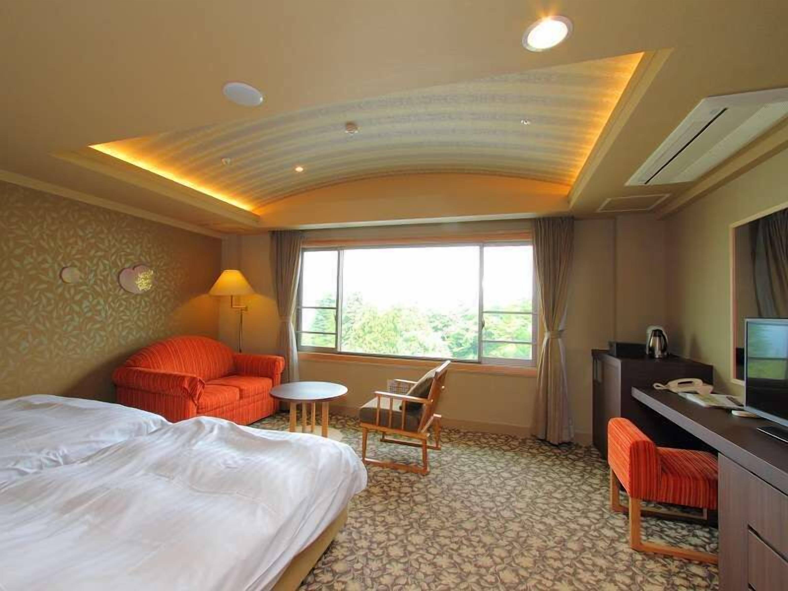 Een hotelkamer met een bed, een bank, een bureau, een stoel en een groot raam.