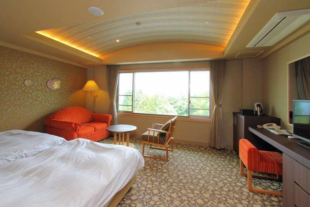 A hotel room with a bed, a sofa, a desk, a chair, and a large window.