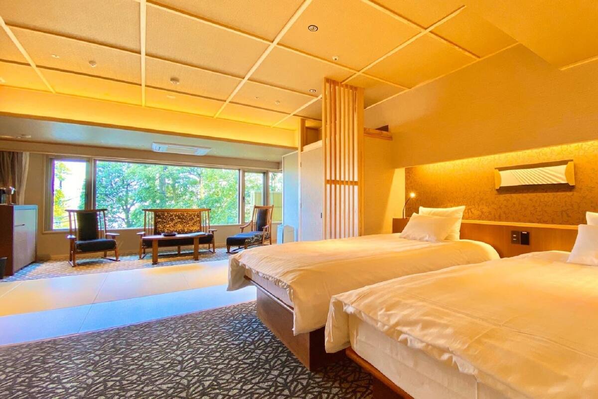 A hotel room with two beds, a desk, a chair, and a view of the outdoors.